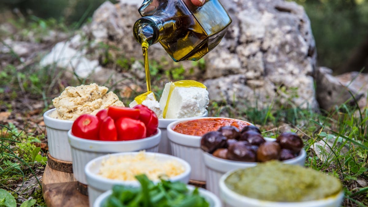 Outdoor picnic with various Mediterranean spreads, herbs, and olive oil drizzle.