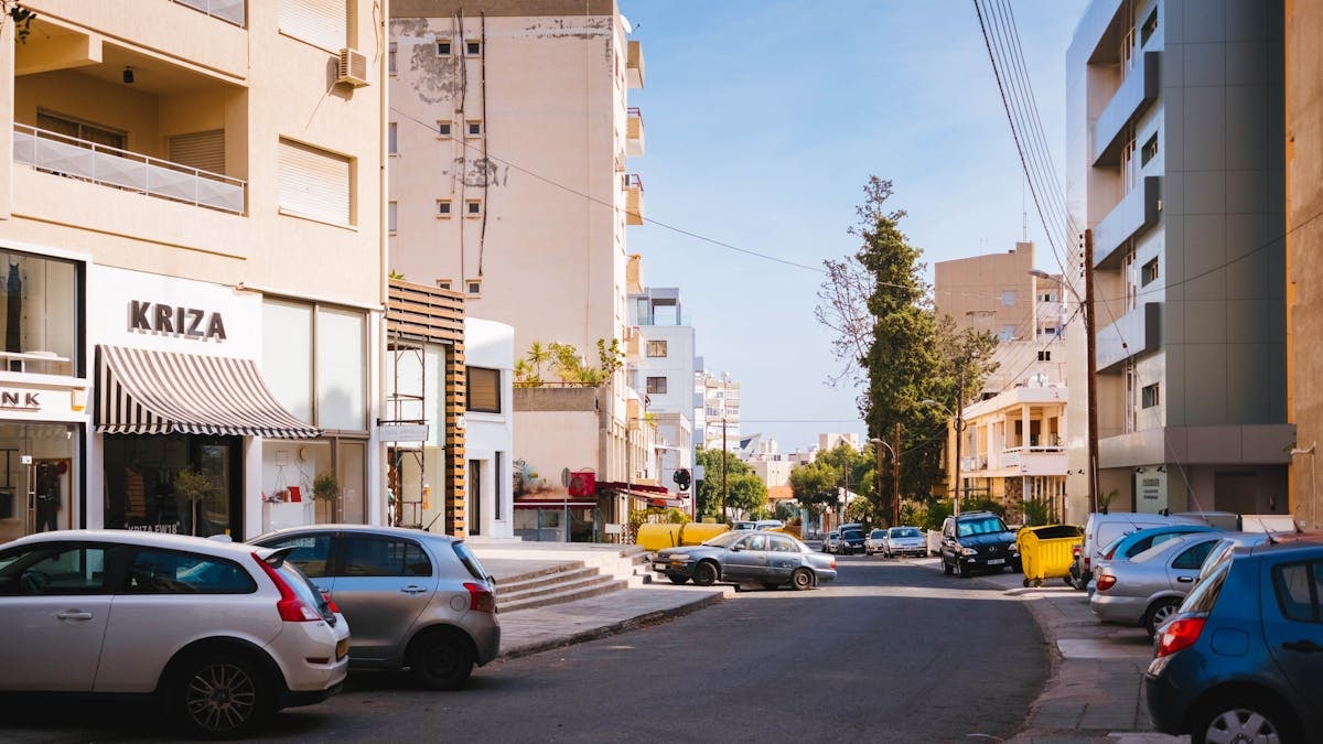 Sunlit street in a Mediterranean city with cars and modern architecture.